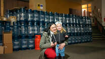 A mother and her small child in front of emergency supplies provided by the IRC and EU